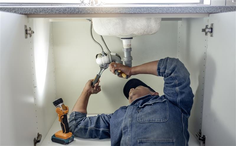 Plumber repairing pipes beneath a bathroom sink in Wildomar