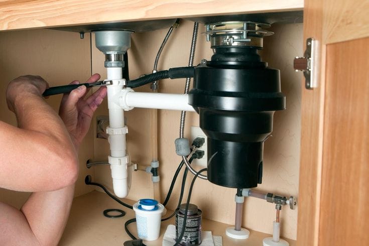 Plumber installing a garbage disposal beneath a kitchen sink in Wildomar