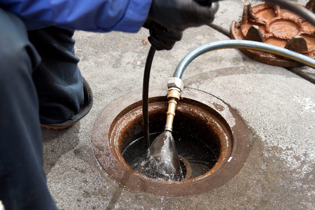 Plumber hydro jetting a sewer line through a manhole in Wildomar