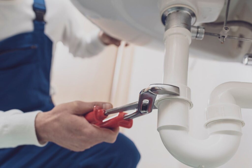 Plumber repairing a white drain pipe beneath a sink in Wildomar