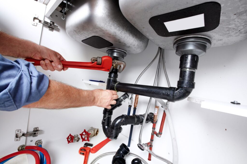 Plumber repairing drain pipes beneath a kitchen sink in Wildomar